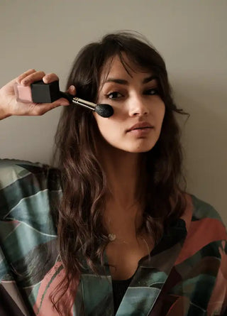 A woman applying makeup with a brush and compact.
