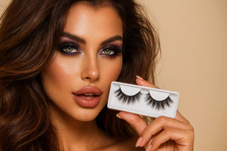 A woman modeling a pair of false eyelashes in their packaging.