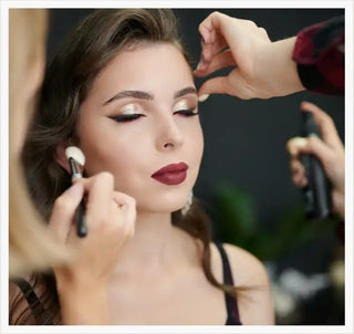 A young woman receiving professional makeup application, featuring dramatic winged eyeliner, shimmer eyeshadow, and deep red lipstick.